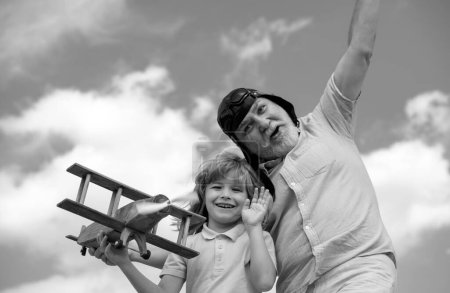 Téléchargez les photos : Grand-père drôle et fils jouant avec avion en bois sur fond de ciel d'été. Enfant garçon avec des rêves de voler ou de voyager. Famille générationnelle - en image libre de droit