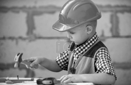 Foto de Un chico con sombrero duro sosteniendo el martillo. Niño pequeño ayudando con herramientas de juguete en el sitio de construciton. Niños con herramientas de construcción. Constructor y reparador de niños constructor - Imagen libre de derechos