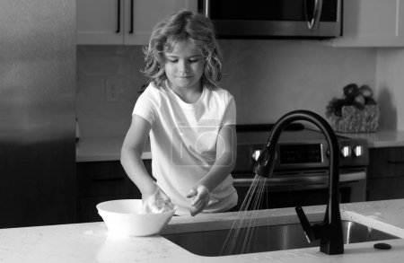 Téléchargez les photos : Nettoyage enfant vaisselle avec éponge. Du matériel de nettoyage. Aide à nettoyer. Tâches ménagères. Il lave la vaisselle. Petit garçon qui lave la vaisselle dans la cuisine intérieure. Enfant aidant ses parents avec les travaux ménagers - en image libre de droit