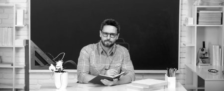 Photo for Young modern male teacher waiting for students. Teacher in casual clothes at blackboard with copy space in class at school - Royalty Free Image