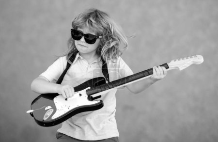 Photo for Funny child with blonde curly hair playing guitar on beige yellow background. Child musician playing the guitar like a rockstar outdoor. Kid boy rock musician with guitar - Royalty Free Image