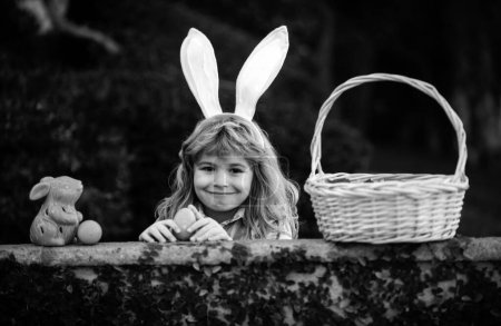Foto de Feliz día de Pascua. Niño con orejas de conejo. Niño cazando huevos de Pascua en el patio trasero - Imagen libre de derechos