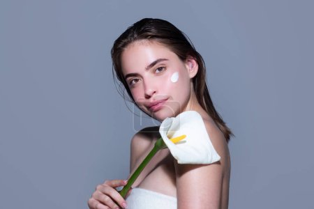 Young woman applying body cream on studio background. Beauty routine. Studio face of a beautiful woman with perfect skin and flower. Wrinkle cream. Concept of beauty