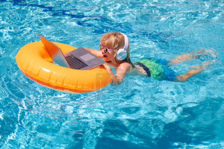 Téléchargez les photos : Travailler à l'extérieur avec ordinateur portable dans la piscine. Enfant travaillant sur un ordinateur portable de la piscine. Affaires d'été - en image libre de droit