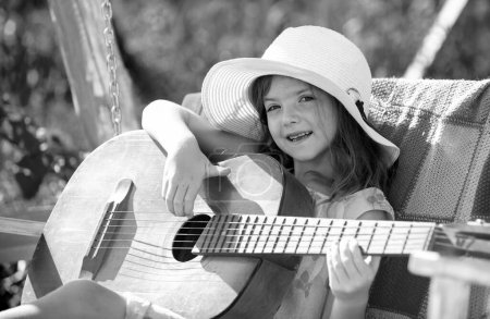 Téléchargez les photos : Musique et chansons pour enfants. Petit enfant jouant de la guitare. Petite fille à la mode. École de guitare musicale pour enfants. Enfant souriant jouant à l'extérieur en été - en image libre de droit