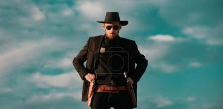 Photo for Sheriff in black suit and cowboy hat, banner. Wild west, western, man with vintage pistol revolver and marshal ammunition - Royalty Free Image