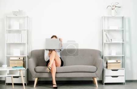 Photo for Young attractive sexy secretary in office. Beautiful secretary legs. Seductive sexy secretary freelancer with laptop computer and sexy legs sit on sofa in office. Sensual young girl employee - Royalty Free Image