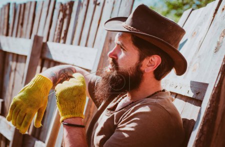 Téléchargez les photos : Portrait de cow-boy occidental. Homme barbu jardinier dans un jardin urbain. Scène rurale. Loisirs de jardinage - en image libre de droit