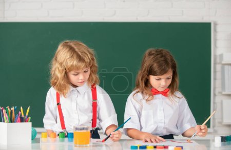 Photo for School children painting with paints color and brush in classroom - Royalty Free Image