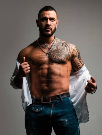 Brutal handsome man with tattooed body. Men tattoo casual fashion. Portrait of brutal handsome male model. Muscular athletic sexy male in unbuttoned shirt. Handsome guy with sexy bare torso