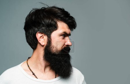 Téléchargez les photos : Portrait semi-tourné profil latéral de l'homme sérieux a la barbe et la moustache, regarde sérieusement, isolé sur gris. Un barbu hippie, à la recherche d'expression. Beau modèle masculin - en image libre de droit