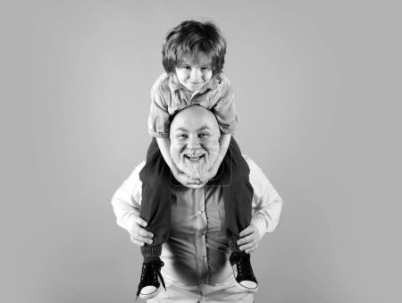 Téléchargez les photos : Grand-père et fils balade en dos de porc avec drôle de visage isolé sur bleu en studio. Grand-père et mignon garçon avec un visage drôle - en image libre de droit