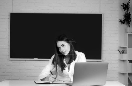 Téléchargez les photos : Portrait d'une jeune étudiante qui étudie en classe sur fond de tableau noir - en image libre de droit