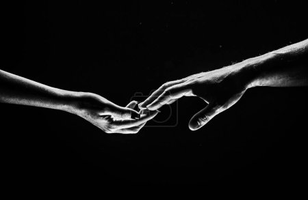 Téléchargez les photos : Deux mains s'étirent, fond noir. Couple amoureux tenant des mains, gros plan. Aide main, soutien, amitié - en image libre de droit
