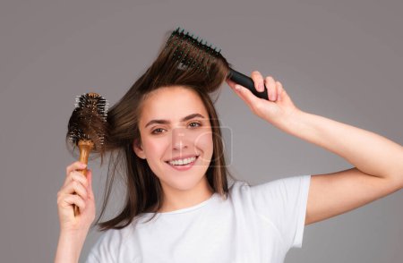 Téléchargez les photos : Jeune belle femme peignage cheveux bruns. Soins capillaires. Belle femme brune brossant les cheveux avec une brosse à cheveux. Brosser les cheveux sains avec un peigne - en image libre de droit