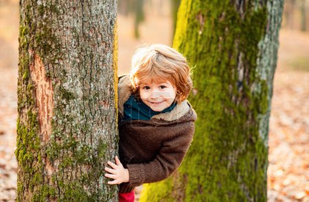 Foto de Retrato de niños de otoño al aire libre. Lindo niño disfrutando trepar al árbol. Niño con ropa otoñal aprendiendo a escalar, divirtiéndose en el bosque o aparcar en un día cálido y soleado. Feliz otoño en la naturaleza - Imagen libre de derechos