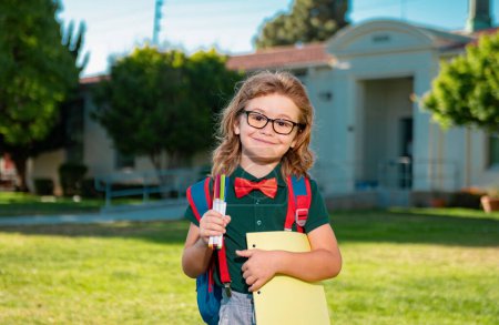Foto de Un pequeño y sonriente libro de mochilas. Retrato de un joven feliz fuera de la escuela primaria. Cara de primer plano de alumno feliz al aire libre. Chico nerd divertido - Imagen libre de derechos
