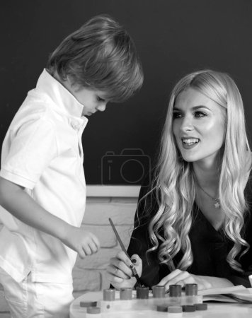 Photo for Mother and two son together draw, paint. Mom helps the child boy. Teacher helping school kids in classroom at school - Royalty Free Image