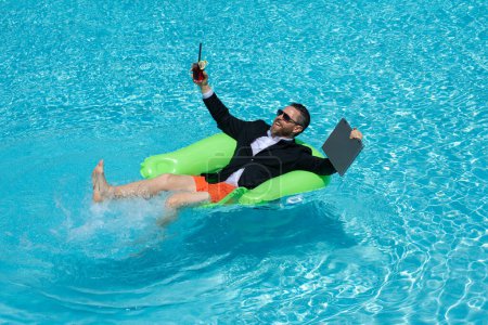 Photo for Freelance work, distance online work, e-working. Summer business. Business man in suit drink summer cocktail and using laptop in pool. Businessman dreams on summer business in swimming pool water - Royalty Free Image