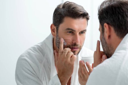 Beauty man applying face cream. Skincare cream, skin anti-aging wrinkle effect. Man applying moisturizer cream on skin. Skin care, cosmetic cream treatment for male face. Male skin care beauty