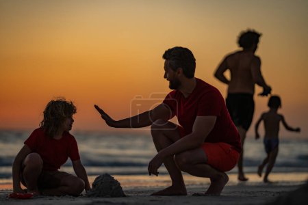 Foto de Niño y padre construyendo un castillo de arena. Padre e hijo jugando en la playa. Padre e hijo jugando en la arena en la playa tropical al atardecer. Castillo de arena. Padre con hijo en el mar. Día de los padres - Imagen libre de derechos