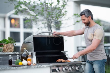 Photo for Barbecue concept. Middle aged hispanic man in t-shirt for barbecue. Roasting and grilling food. Roasting meat outdoors. Barbecue and grill. Cooking meat in backyard - Royalty Free Image