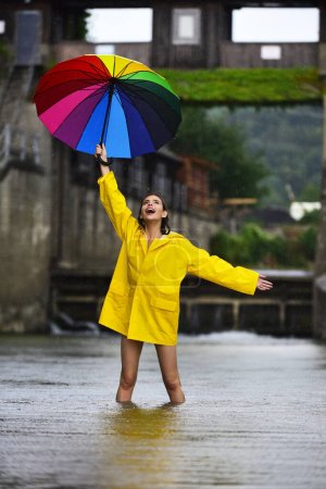 Téléchargez les photos : Jour de pluie. Femme excitée drôle dans parapluie tenue imperméable avec gouttes d'eau de pluie. Fille en imperméable sous les gouttes d'eau tombantes en saison des pluies. Femme avec parapluie. Pluie estivale. Météo pluvieuse - en image libre de droit