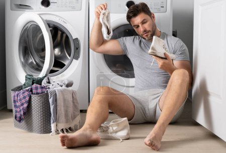 Photo for Man loading clothes into washing machine in laundry room. Middle age man putting laundry in to washing machine scared and amazed with open mouth for surprise, disbelief face with dirty clothes - Royalty Free Image