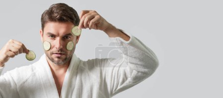 Cara limpia, cuidado facial, concepto de tratamientos faciales. Hombre de mediana edad con máscara de pepino aislado en el fondo del estudio. Pepino para cosméticos máscara de piel. Mascarilla facial con pepino. Spa, dermatología. Banner