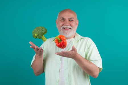 Photo for Healthy Senior man throw up broccoli and pepper. Old mature man with vegetables in studio. Healthy vegetables, pepper and broccoli for dieting. Healthy food. Vegan Mature man, healthy lifestyle - Royalty Free Image