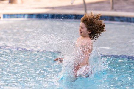 Téléchargez les photos : Il saute dans la piscine. Éclaboussures d'enfants dans la piscine d'eau d'été. Un petit plongeon dans la piscine. Heureux petit garçon qui saute dans l'eau. Saut d'enfant dans la piscine et éclaboussures d'eau - en image libre de droit