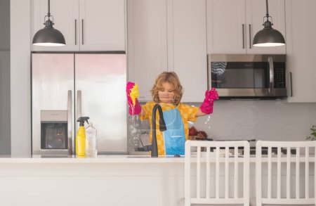 Téléchargez les photos : Ménage, tâches ménagères. Lave-vaisselle pour enfants dans la cuisine intérieure. Un enfant qui aide au ménage. Nettoyage et entretien ménager concept. Poussière et gants pour enfants pour le nettoyage - en image libre de droit
