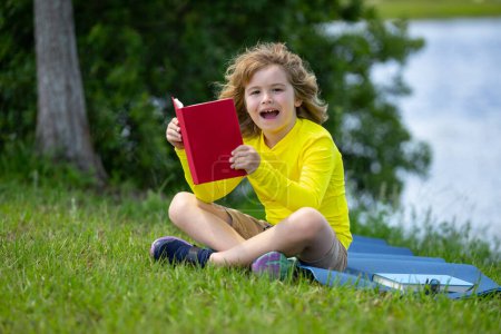 Photo for Child with a book. Early education for kids. Summer vacation with book. Outdoor homework. Summer camp with book. Kids learning and education concept. Kid sitting on grass and reading a book - Royalty Free Image