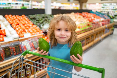 Téléchargez les photos : Joyeux petit enfant avec des fruits et légumes à l'épicerie. Alimentation saine pour les jeunes familles avec enfants. Enfant heureux avec panier plein de légumes frais. Enfants à l'épicerie ou au supermarché - en image libre de droit