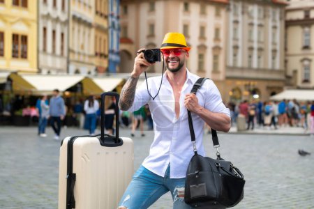 Foto de Hombre viajero con gafas de sol, sombrero y cámara. Hombre de negocios en viaje de negocios caminando con bolsa de viaje en la calle de la ciudad. Viajante hombre de negocios - Imagen libre de derechos