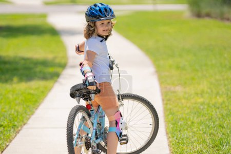 Téléchargez les photos : Enfant à vélo. Petit garçon en casque à vélo le long de la piste cyclable. Joyeux petit garçon en vélo. Enfant dans le casque de protection pour vélo à vélo - en image libre de droit