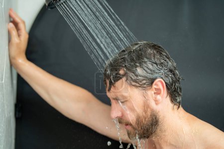 Foto de Hombre hispano lavando el pelo en el baño. Cabezal de ducha en la bañera. Cara masculina en la ducha. Hombre duchándose en el baño. Un tipo duchándose. Concepto de baño. El hombre está bajo gotas de agua en el baño - Imagen libre de derechos