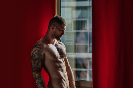 Photo for Sexy naked young man in living room on window curtains. Nude male body. Sexy model. Young muscular man with sexy body. Bare chest. Muscular male torso, bare shoulders - Royalty Free Image