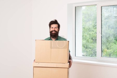 Téléchargez les photos : Heureux homme joyeux portant boîte en carton le jour du déménagement. Livreur chargeant des boîtes en carton pour déménager dans un appartement - en image libre de droit