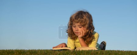 Téléchargez les photos : Mignon enfant lire des livres à l'extérieur. Bannière de printemps pour en-tête de site Web. Un gamin sérieux lisant un livre au parc. Printemps et enfant. Bannière pour en-tête de site Web - en image libre de droit