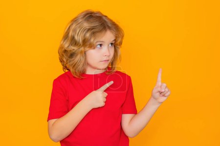 Foto de Niño divertido en camiseta roja apuntando con el dedo sobre fondo de estudio aislado amarillo. Chico divertido apuntando a copyspace, mostrando ofertas promocionales, puntos de distancia - Imagen libre de derechos