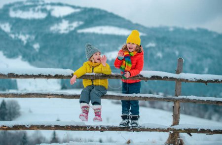 Photo for Funny little children in winter outdoor. Smiling kids friends in frost snowy day outdoor. Two handsome boys an girl resting together in park with snow background. Hapy kids emotions - Royalty Free Image