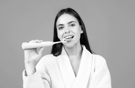 Foto de Joven mujer alegre cepillarse los dientes con cepillo de dientes durante los procedimientos de higiene matutina aislado fondo, retrato facial. Cepillo de dientes eléctrico - Imagen libre de derechos