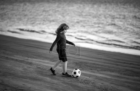 Young soccer player. Kid kicking a football ball on a sandy beach. Sports kid during soccer training
