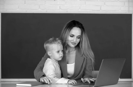 Photo for Mother and son learning. Teacher helping school child in class at school. Little school child son using laptop with mother - Royalty Free Image