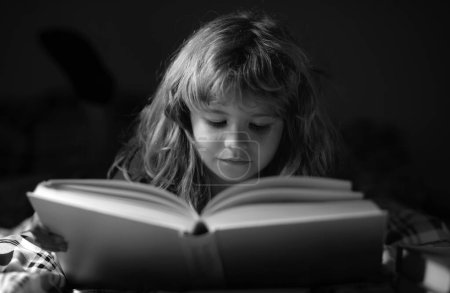 Foto de Lindo niño leyendo un libro. Niño con libro abierto. Lección de escuela en casa. Un niño concentrado en la cama leyendo libros en casa. El desarrollo infantil de la fantasía - Imagen libre de derechos