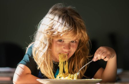 Cute child eating breakfast at home. Cute little kid eating spaghetti pasta at home. Close up portrait of funny kid eating noodles pasta