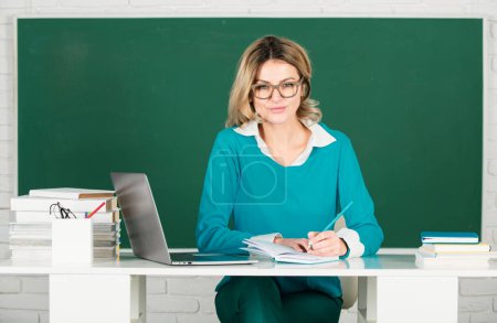 Foto de Sensual student woman in eyeglasses near blackboard. Sexy girl sit on table on chalkboard. Attractive female teacher in college. education, high school and people concept - Imagen libre de derechos