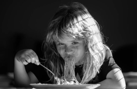 Téléchargez les photos : Enfant mangeant sur fond flou. Un petit garçon affamé qui mange. Nourriture maison pour les enfants. Nourriture savoureuse, enfant désordonné manger des spaghettis. - en image libre de droit
