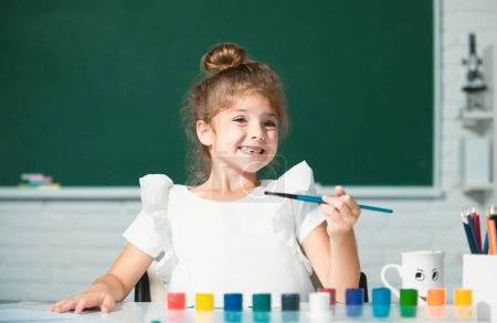 Foto de Cute little preschooler child girl drawing at school. Child girl painting on elementary school. Funny kids emotions - Imagen libre de derechos